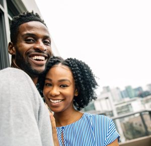 Happy black couple, standing together on the balcony, hugging, overlooking a beautiful city view